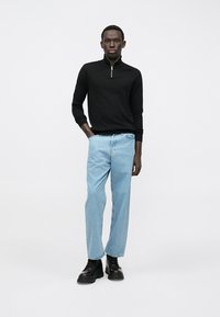 Črn pulover z zadrgo, svetlo modri ravni kavbojki in masivni črni škornji. Obleka ima sproščen silhuet in minimalističen dizajn.