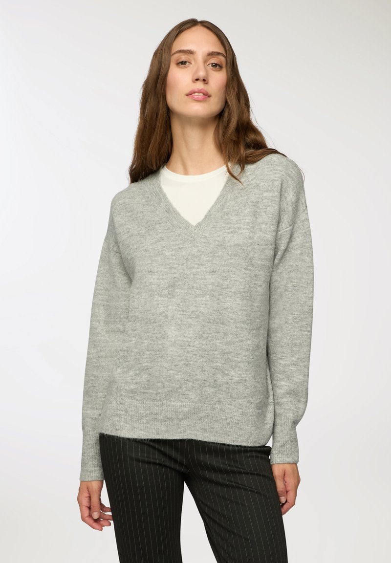 Maglione v-neck grigio chiaro con maniche lunghe, realizzato in un tessuto morbido e testurizzato, abbinato a pantaloni neri a righe sottili. Design semplice e moderno.