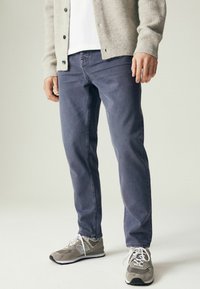 Jeans gris à coupe droite, associés à un cardigan en tricot gris clair. Chaussures de sport grises avec des lacets blancs et une surface texturée.