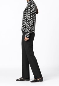 Maglietta a maniche lunghe in bianco e nero con un motivo a catena, abbinata a pantaloni neri dritti e mocassini neri con un accento decorativo.