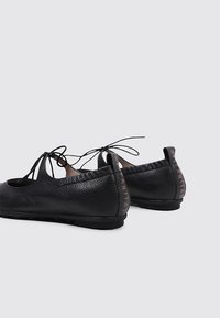 Bailarinas de cuero negro con un acabado texturizado, diseño de cordones y suela flexible. Marca destacada en el tacón.