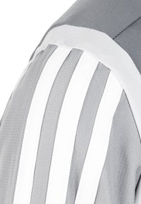 Camiseta atlética gris con distintivas rayas blancas, tejido texturizado y costuras suaves, que destaca un diseño en capas en el hombro.