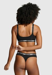 Schwarzer Sport-BH und Tanga mit verstellbaren Trägern und einem weißen Logo-Band. Der Stoff wirkt glatt und hat ein körpernahes Design.