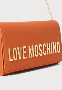 Geantă de mână din piele ecologică de culoare portocalie, cu o formă rectangulară, având inscripția cu litere aurii "LOVE MOSCHINO" pe față și o curea din lanț.