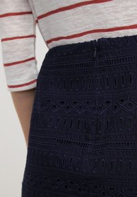 Jupe bleu marine avec des motifs géométriques brodés ; tissu texturé avec des découpes et un design cousu ; détail de taille élastique visible.