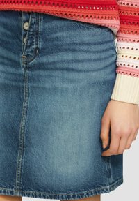 Leren rok, lichtblauw, A-lijn vorm, met knopen aan de voorkant en subtiele vervaging. Heeft een rechte zoom en gestikte details langs de naden.