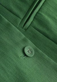 Gros plan d’un tissu vert avec un bouton rond assorti cousu avec quatre trous près d’une couture ou d’un pli plié.
