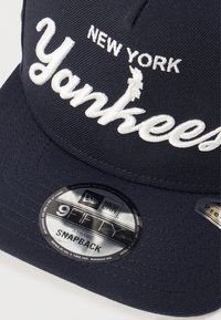 Casquette de baseball marine avec le texte "New York Yankees" brodé en blanc, fermeture snapback, étiquette New Era 9Fifty, couronne structurée et visière plate.