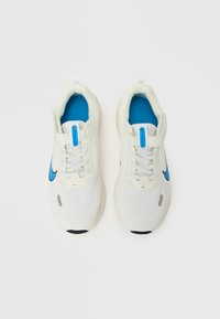 Nike futócipő fehér hálós felsőrésszel, kék részletekkel és texturált talppal. Fűzőzáras és húzófüllel könnyű felvételhez.