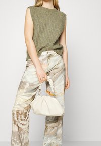 Olijfgroene geribbelde mouwloze top gecombineerd met crèmekleurige gemarmerde wijde broek en een kleine witte handtas met een gedraaide handgreep.