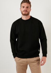 Zwarte katoenen sweatshirt met ronde hals, ribgebreide manchetten en tailleband. Bevat een klein logotag aan de onderzijde. Eenvoudig, rechtgesneden ontwerp.