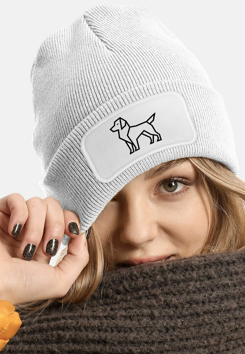 White knitted beanie featuring a rectangular patch with a black outline of a dog. The ribbed texture adds depth.