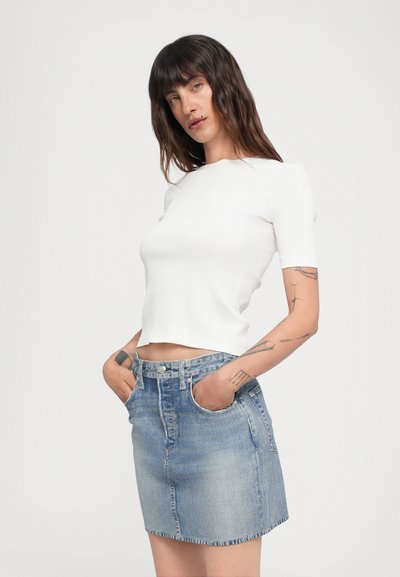 Vit kortärmad crop top tillsammans med en ljusblå denim minikjol med fem fickor och knäppning fram.