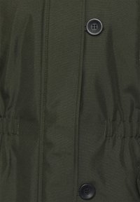 Oliwkowa kurtka z gładkiego, teksturowanego materiału, zapinana na guziki z przodu, z elastycznymi marszczeniami w talii dla regulowanego dopasowania.