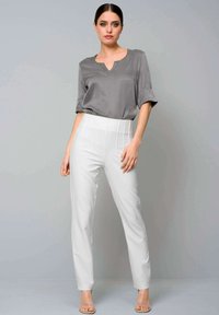 Grey short-sleeve blouse with a V-neck, paired with high-waisted white trousers featuring pleats. Smooth texture and fitted design.