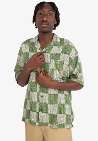 Camisa de botón de manga corta en verde y blanco con un patrón de vetas de madera en cuadrados alternos. Con un bolsillo en el pecho y un corte relajado.