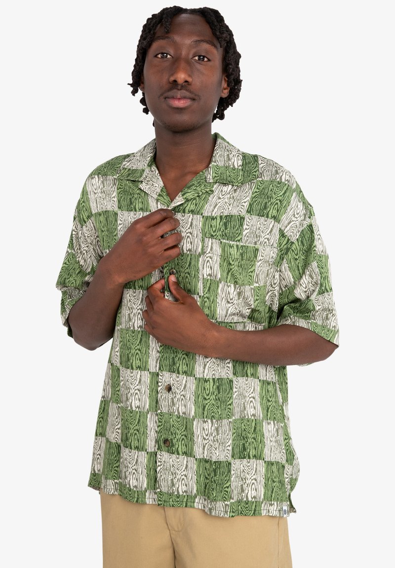 Camisa de botón de manga corta en verde y blanco con un patrón de vetas de madera en cuadrados alternos. Con un bolsillo en el pecho y un corte relajado.