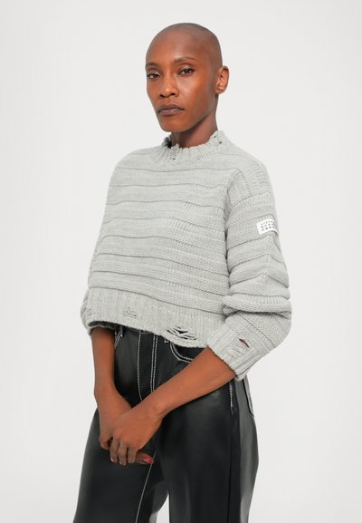 Ljust grått kort stickat tröja med texturerade horisontella ränder, ribbad krage och rullade ärmar. Kombinerat med svarta läderbyxor.