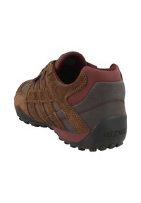 Sneaker in suede marrone e grigio con accenti rossi, caratterizzato da una superficie texturizzata, un design traspirante e una suola in gomma nera con pattern antiscivolo.