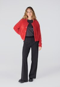 Rode fuzzy cardigan met ronde halslijn, knoopsluiting, gecombineerd met een grijze t-shirt. Zwarte broek met wijde pijpen en stevige zwarte platform schoenen.