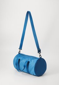 Blaues Textil-Duffelbag, zylindrische Form, mit zwei Griffen und einem verstellbaren Tragegurt. Glatte Textur mit einem Reißverschluss oben.