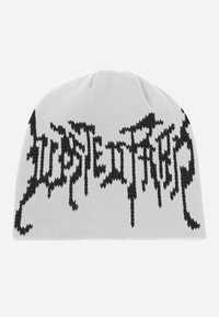 Hvid strikket hue med sort grafisk tekst med takkede kanter, der fremhæver et dristigt, stiliseret design. Blød tekstur, rund top.