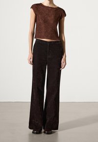 Ruskea, pintakuvioitu keskipitkä neulepaita yhdistettynä korkeavyötäröisiin, tummanruskeisiin corduroypö trousers-housuihin. Mallilla on jalassaan mustat nilkkurit.