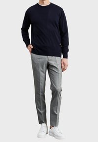 Navy knit sweater, gray patterned trousers, and white sneakers. Sweater features a crew neckline and ribbed cuffs; pants have front pleats.