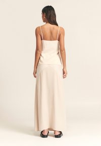 Beež värvi varrukateta topp õhukeste rihmadega, millele on lisatud pikk, voolav beež seelik, sileda tekstuuri ja minimalistliku disainiga. Mustad sandaalid.