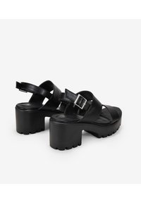 Sandalias de plataforma de cuero negro con tacón de bloque, tiras cruzadas, hebilla ajustable y suela texturizada para mayor agarre.
