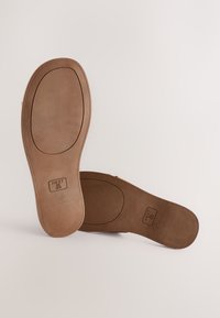 Semelles intérieures brunes avec une texture lisse, une forme ovale et des semelles plates. Présentent un logo estampé et des détails de taille pour une identification facile.