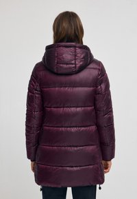 Vadderad parka-jacka i mörk plommonlila, med huva, horisontella sömmar och en något blank yta. Dragsko vid fållen för justering.