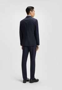 Mörkblå skräddarsydd kostym med en enknäppt kavaj och raka byxor, tillverkad av texturerat tyg, med subtila sömdetaljer.