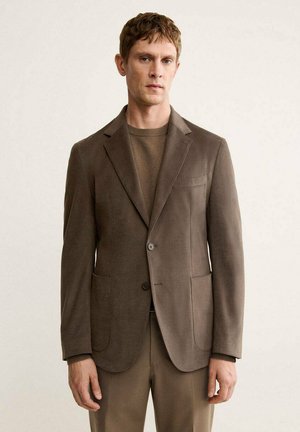 Blazer marron texturé avec deux poches avant, fermeture à un bouton, coupe ajustée, porté sur un pull brun. Design simple, sans motifs.