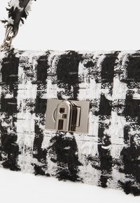 Schwarz-weiß gewebte Tweed-Tasche mit einem glänzenden silbernen Verschluss und texturierter Oberfläche. Verfügt über ausgefranste Kanten und einen Kettenriemen.