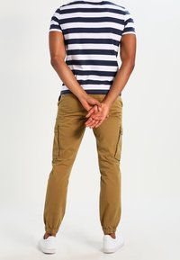 Gestreept marineblauw-wit shirt met korte mouwen, beige cargobroek met elastische boorden en zijzakken, gecombineerd met witte sneakers.