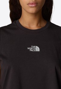 Zwarte katoenen t-shirt met een klein, wit geborduurd logo van "The North Face" op de linkerborst en een klassieke ronde hals.