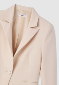 Blazer beige con rever a scollo, chiusura con un bottone e due tasche frontali; tessuto liscio con design sartoriale.