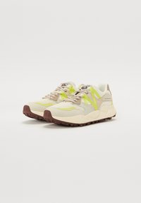 Sneaker mit einem oberen Teil aus beigem Mesh, limettengrünen Akzenten und brauner Gummisohle, die ein strukturiertes Design und kontrastierende Schichten für Unterstützung bieten.