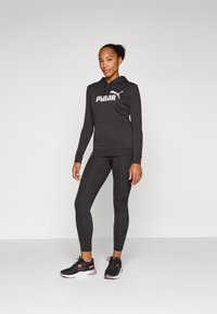 Felpa nera con logo Puma bianco, abbinata a leggings neri e scarpe da ginnastica nere con dettagli rosa. Design semplice e aderente.