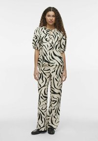 Conjunto de dos piezas que incluye una blusa de manga corta y pantalones de pierna ancha en una base crema con rayas abstractas negras. Tejido suave y texturizado.