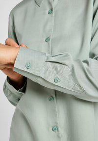 Chemise bleu clair à boutons avec une texture lisse, dotée d'un col, de manches longues et de boutons assortis bleu clair.