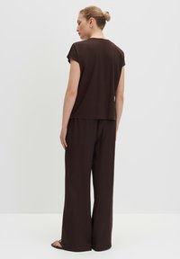 Braunes Kurzarm-Oberteil und weit geschnittene Hose aus glattem Stoff. Das T-Shirt hat eine lockere Passform; die Hose verfügt über einen elastischen Bund.