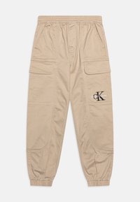 Beige cargo kalhoty s elastickým pasem, několika kapsami a staženými manžetami. Na levé straně je potisknuté logo.