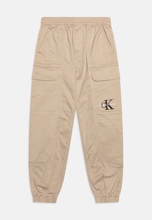 Beige cargo kalhoty s elastickým pasem, několika kapsami a staženými manžetami. Na levé straně je potisknuté logo.