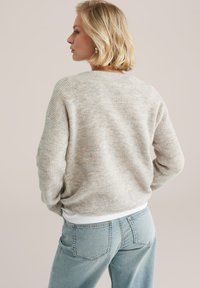 Pull en tricot beige clair à texture côtelée, avec un grand col, des épaules tombantes, associé à un jean taille haute bleu clair.