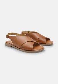 Pruunid nahast sandaalid ristirihmadega, avatud varvastega ja slingback disainiga. Omavad tasast tallat ja väikest kuldset pandlat reguleerimiseks.