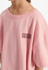 Lyserød bomulds-t-shirt med afslappet pasform, bred halsudskæring og korte ærmer. Har et "AMERICAN VINTAGE" logo trykt i mørkebrun.