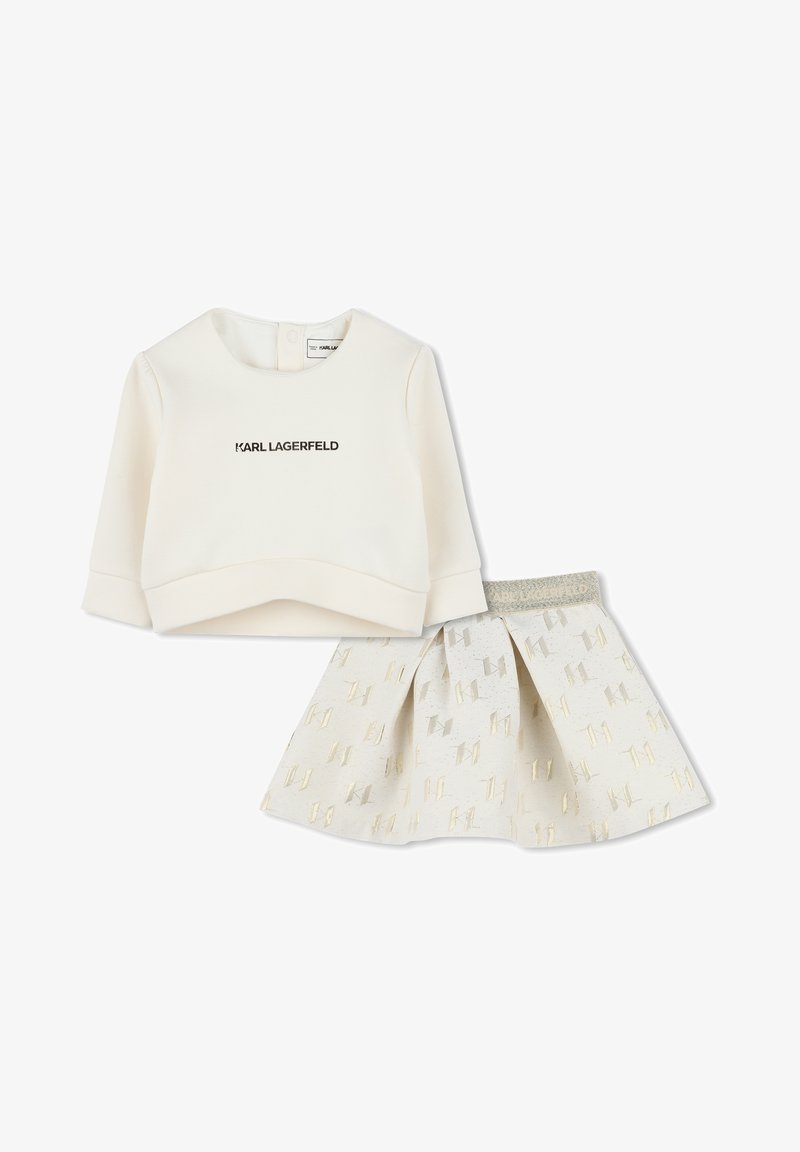 Witte katoenen sweatshirt met zwarte "KARL LAGERFELD" opdruk, gecombineerd met een witte rok met gouden geometrische patronen en een grijze tailleband.