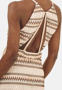 Vestido de punto beige con detalle de espalda al aire, que presenta un patrón geométrico en marrón y naranja, y tirantes finos.